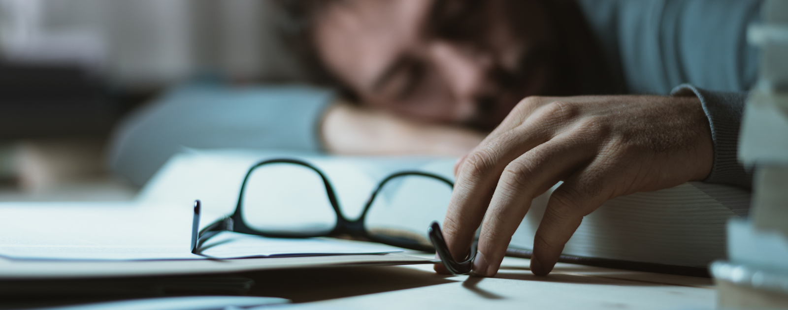 Pessoa a dormir em cima de um livro enquanto segura uns óculos