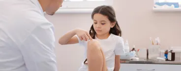 menina indica ao médico onde costuma sentir dor nas pernas