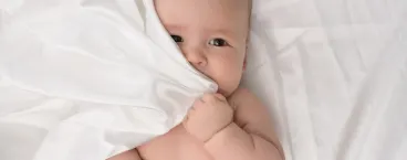 bebé a tapar parte da cara com o lençol