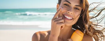 mulher sorridente na praia a aplicar protetor solar 