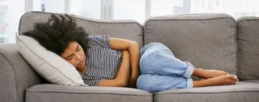 mulher deitada no sofá com dores abdominais