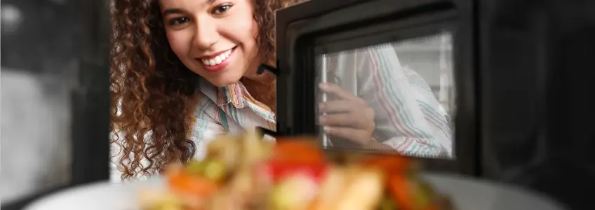 mulher abre porta do microondas e olha para prato de comida aquecida