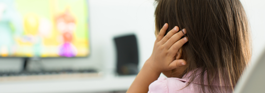Criança com autismo com as mãos a tapar as orelhas a ver televisão