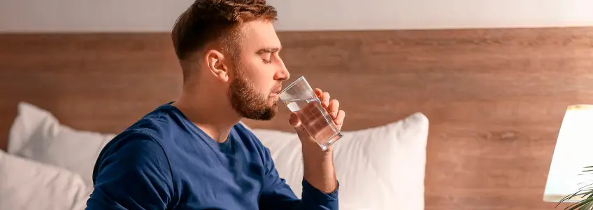 homem a beber água sentado na cama