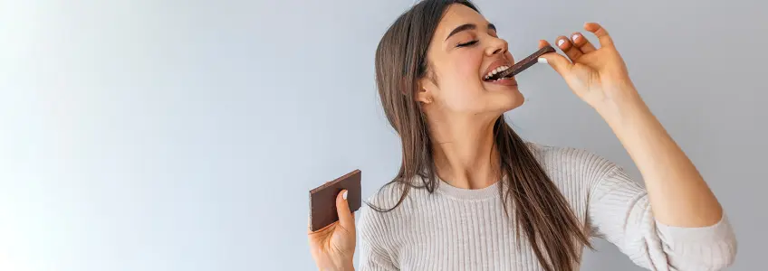 rapariga a sorrir enquanto dá uma trinca num chocolate