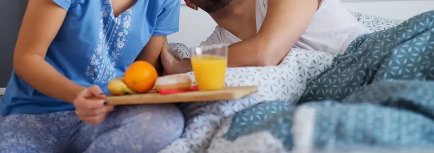 mulher a levar pequeno almoço à cama com um tabuleiro de pão, fruta e sumo de laranja