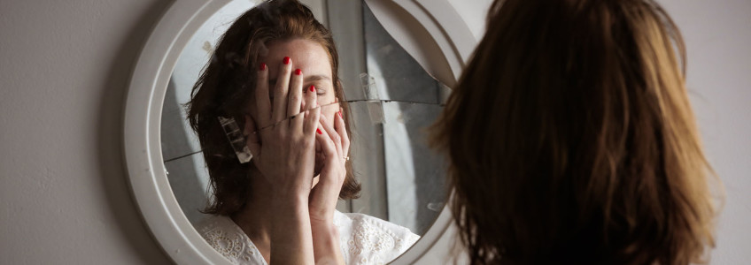 mulher tapa a cara diante de espelho partido