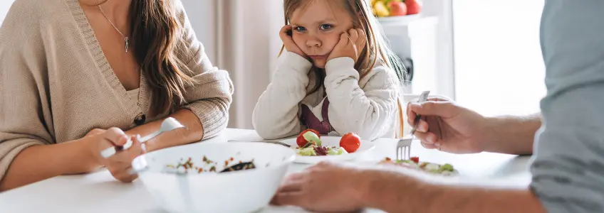 menina sentada à mesa com os pais recusando comer
