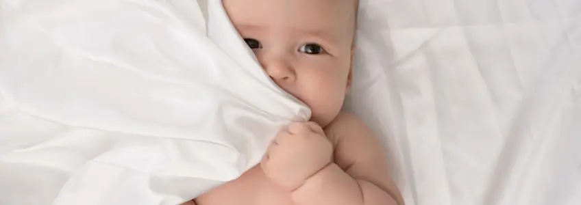 bebé a tapar parte da cara com o lençol