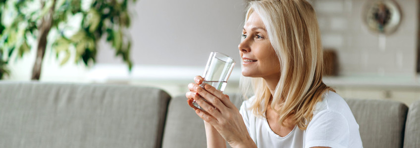 mulher sentada no sofá com copo de água na mão