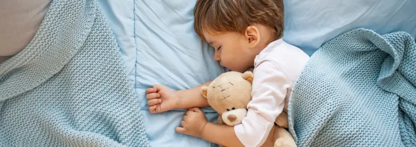 bebé a dormir abraçado a urso de peluche