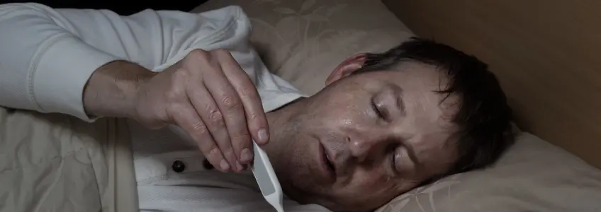 homem deitado na cama a medir a febre com termómetro