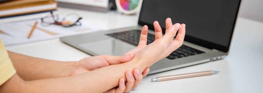 mulher em frente ao computador a massajar a mão