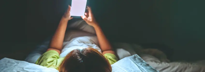 menina deitada na cama a olhar para o telemóvel