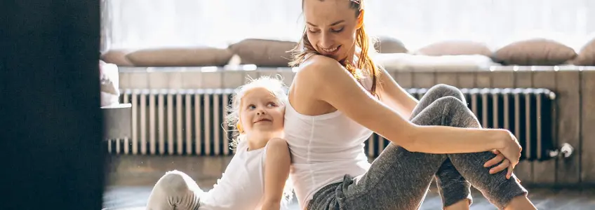 mãe e filha sorriem uma para a outra, sentadas no chão